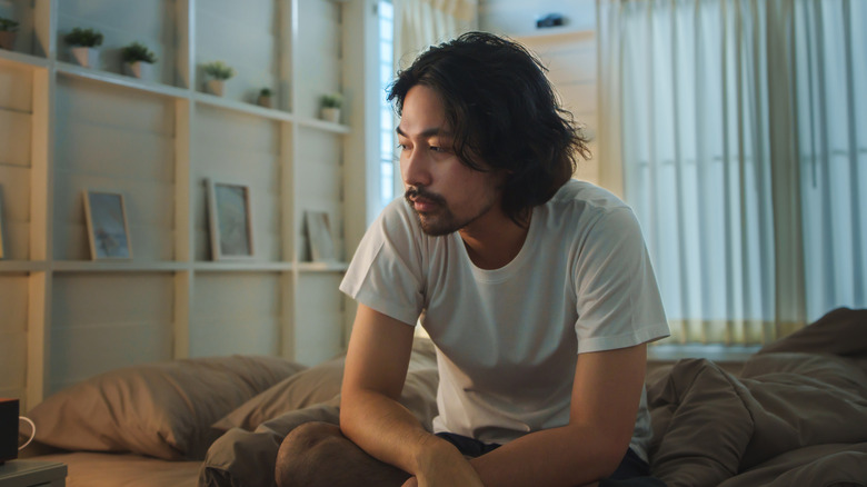 Young man sitting on bed appearing sad and lonely