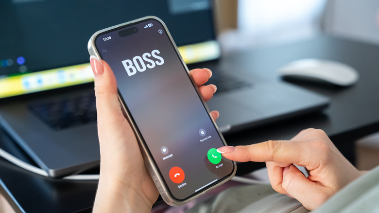 A person holds a smartphone that shows an incoming call from their boss