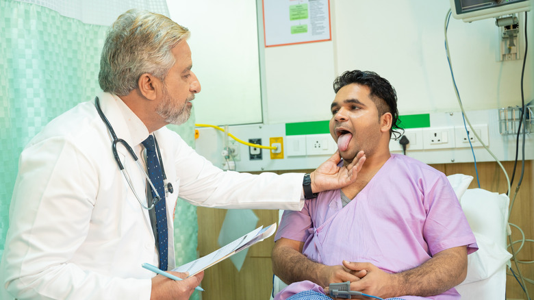 A doctor examining a patient's tongue in hospital bed