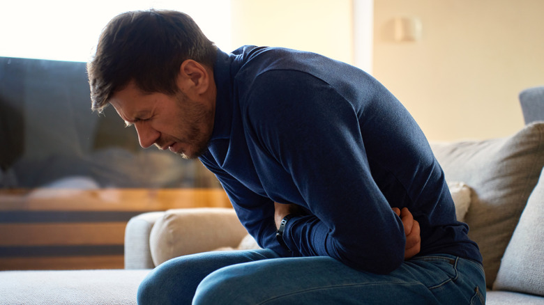 Man sitting on sofa and leaning forward with arms across stomach