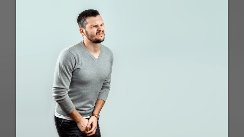 Young man with crossed legs, and holding his pelvic area, implying issues with urinating