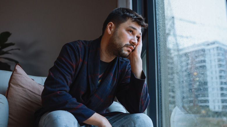 Man appearing to have low energy, looking out of the window