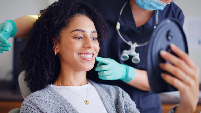 Woman looking in mirror while dentist points to the mouth