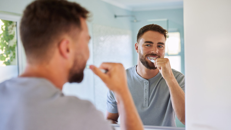 Man brushing teeth while looking in bathroom mirror