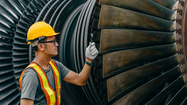 Airplane engineer inspecting jet engine in hard hat and vest