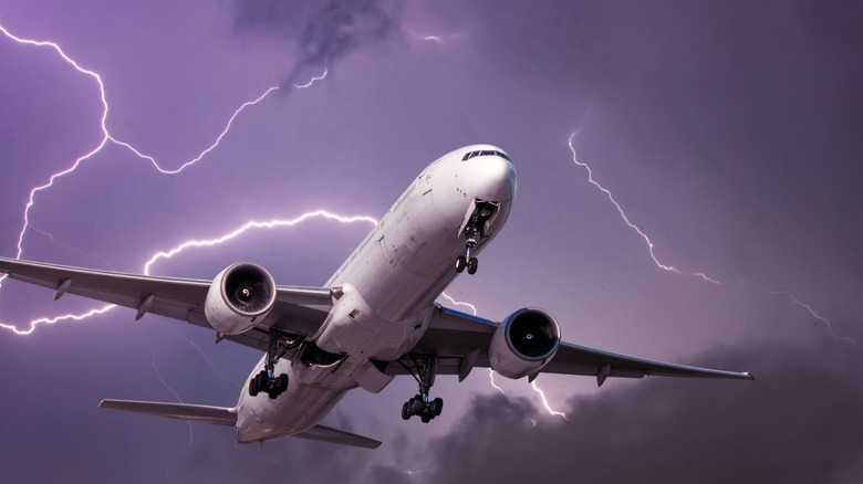 commercial passenger plane flying through storm cloud with lightning surrounding it