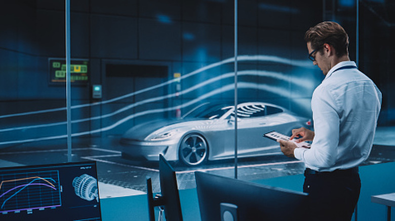 engineer looks at tablet while standing in front of a futuristic car wind tunnel