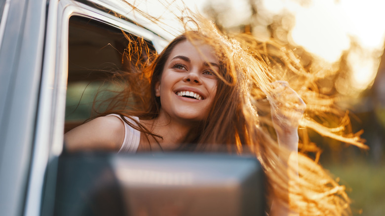 Young woman with head out of car window, smiling while hair blows in wind