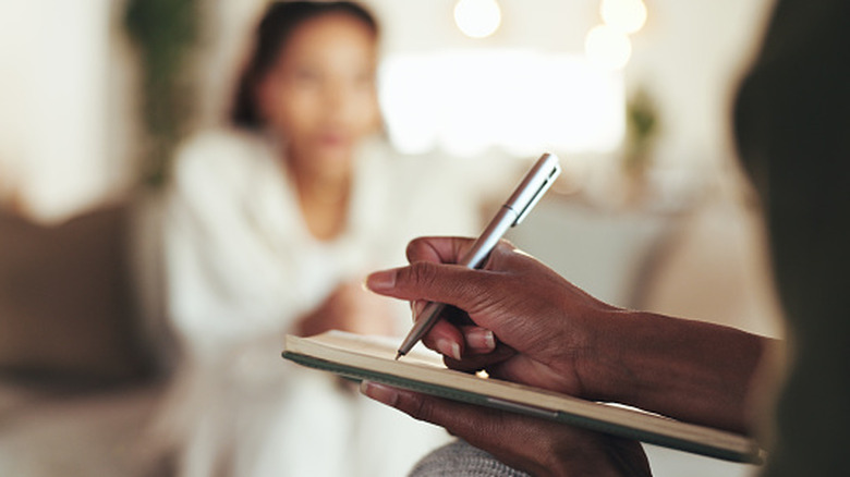 Therapist writing on a clipboard while talking with patient