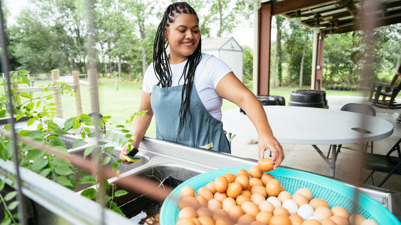 Woman placing an egg in basket next to fresh herbs outdoors