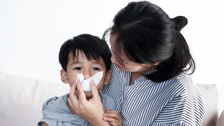 Woman helping a young boy blow his nose with a tissue
