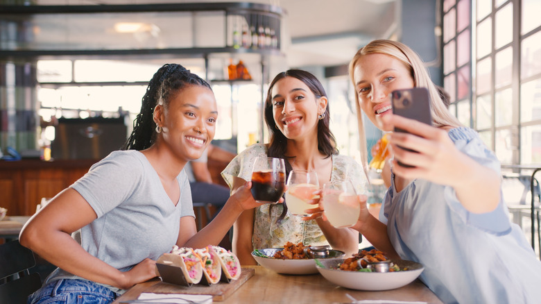Group of female friends posing with drinks and food at a restaurant table