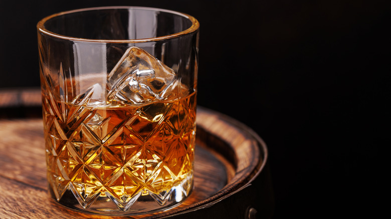 Glass of whiskey with ice sitting on a wooden barrel