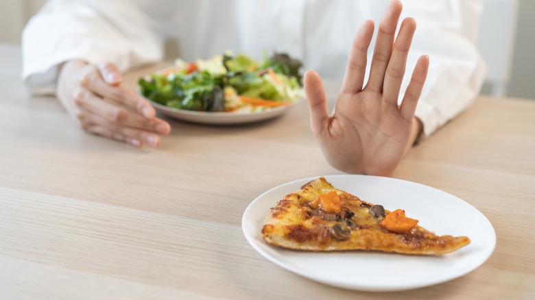 Hand pushing away a slice of pizza in favor of salad