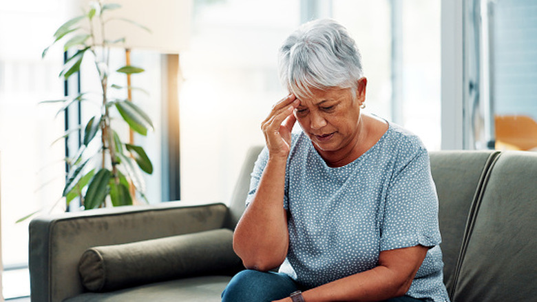 Older woman, holding her head and looking worried