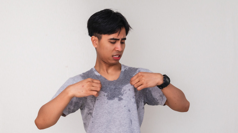 Young Asian male with sweat stains on shirt, grossed-out face
