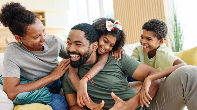 Smiling black family, mother, father, daughter, son, on couch embracing each other