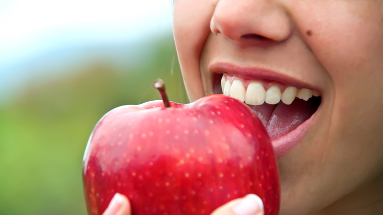 A photo of a woman with her mouth open, getting ready to take a bite out of an apple