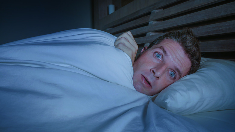 A man in bed looking horrified