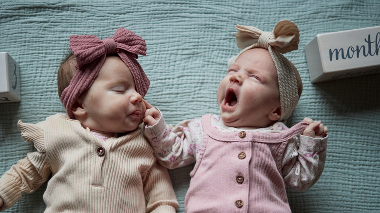 Two infant twins laying side by side, one yawning