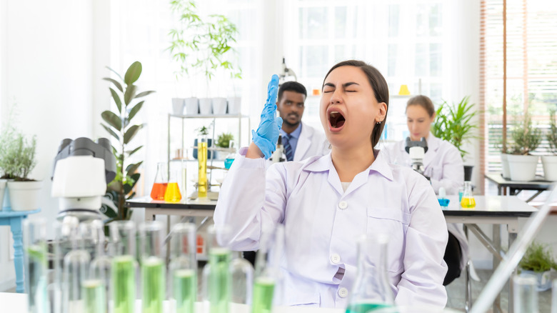 Female scientists yawning in lab, colleagues behind her