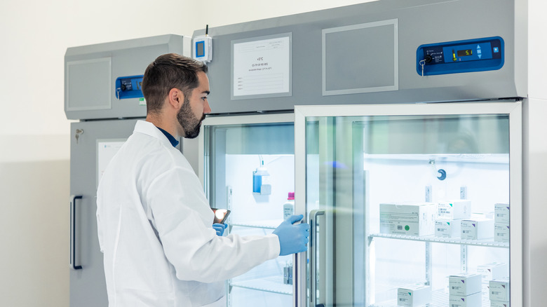 Scientist in white lab coat opening transparent refrigerator door