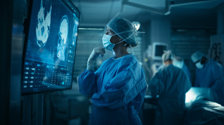 A surgeon observes brain scans on a large screen.