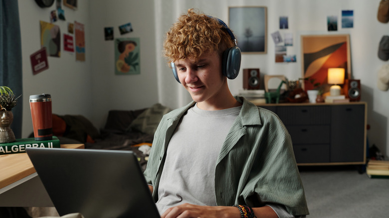 White curly haired male sitting at computer with headphones on smiling