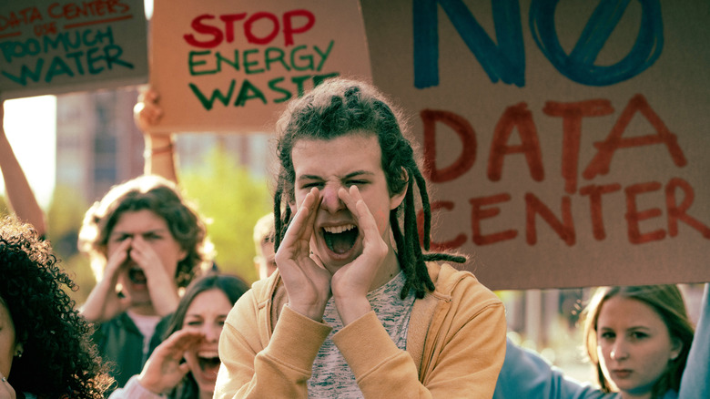 A young adult with dreadlocks shouting through cupped hands at a protest
