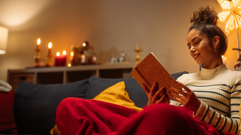 Young woman smiling while reading book with candles lit in the background