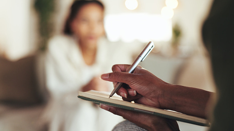 Therapist writing on a clipboard while talking with patient