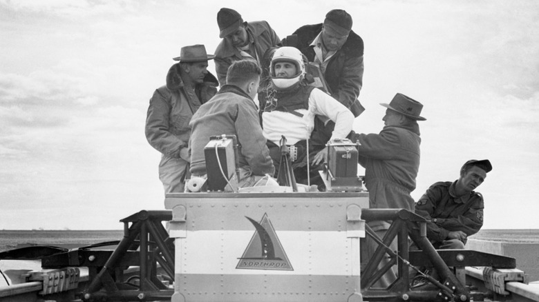 Col. John Stapp, wearing a white helmet, being strapped into rocket sled