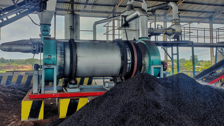 A pile of black biochar in front of production machinery