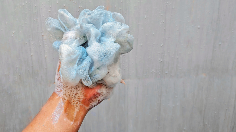Hand holding a blue shower puff with soap suds