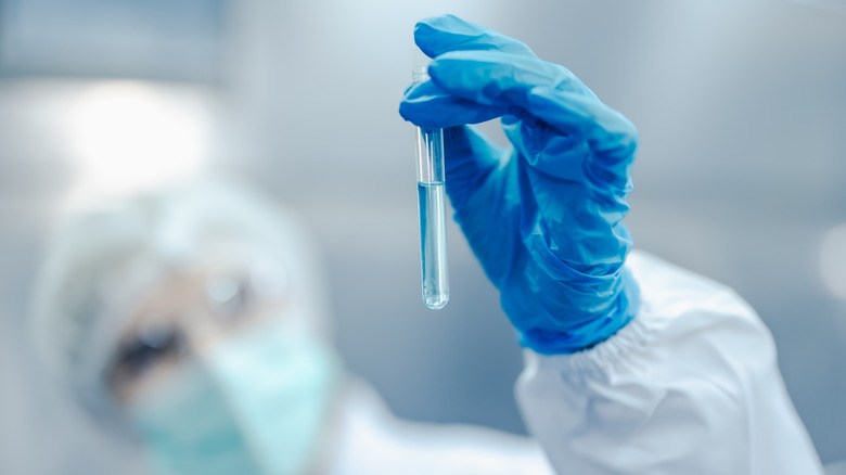 A gloved hand holding up a test tube that contains blue liquid.