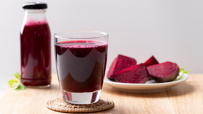 Focus on a glass of beetroot juice with a bottle and slices of beetroot in the background