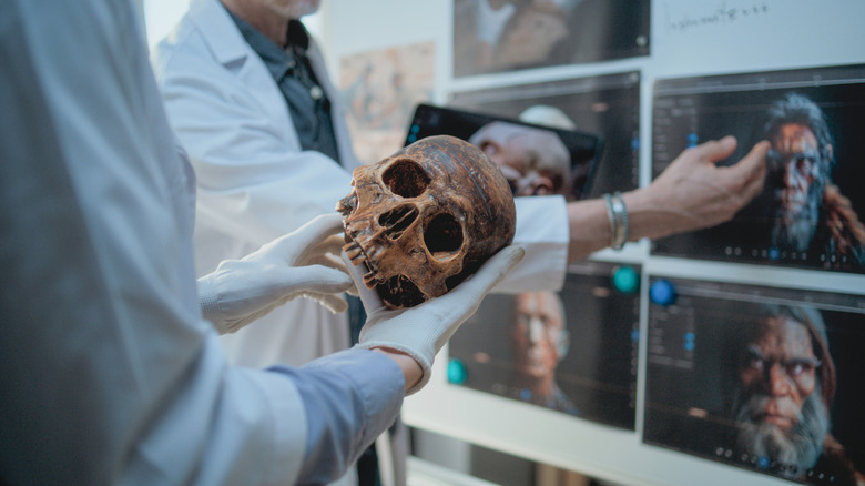 Scientists hold a Neanderthal skull in front of a screen displaying 3-D images renderings of Neanderthal heads.