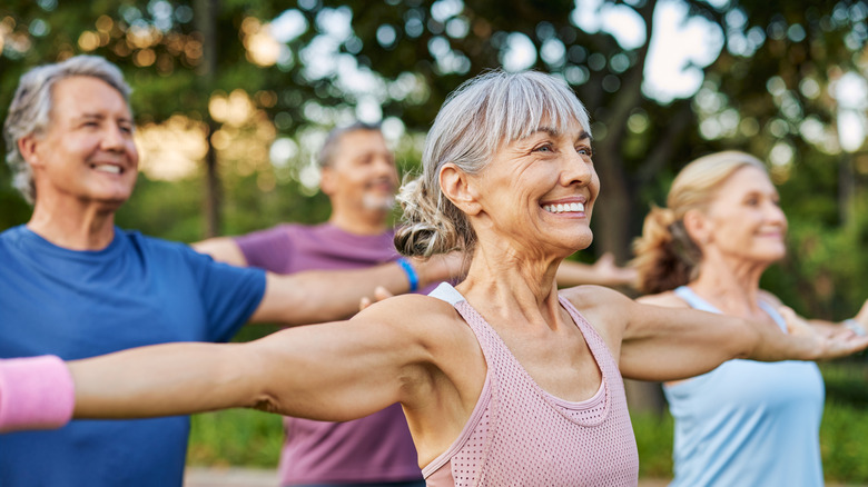 Seniors practicing stretches outdoors with big smiles