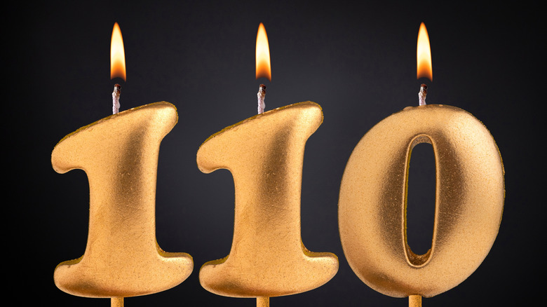 The number "110" in lit, gold candles on a black background
