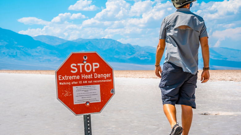 Man walking outdoors past an extreme heat danger sign