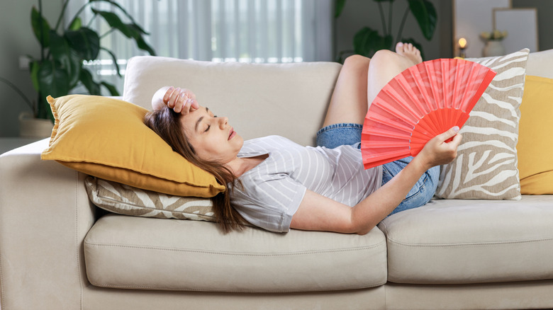 Woman laying on sofa with a fan trying to stay cool
