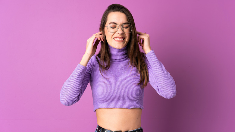 Young woman cringing and covering her ears