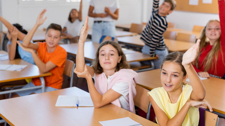 Children in a classroom raising their hands with enthusiasm