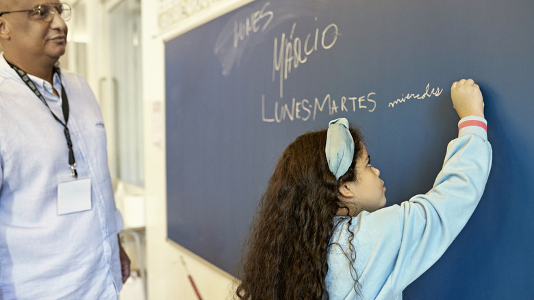 Young girl writing on blackboard while male instructor looks on
