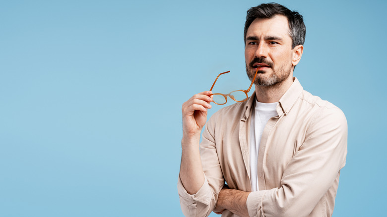 Man staring into the distance, holding the leg of his spectacles to his mouth