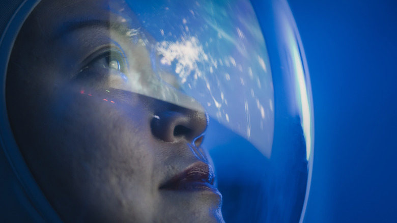 A female astronaut looking at Earth from space through her spacesuit helmet