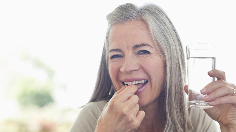 Mature woman taking a pill with a glass of water