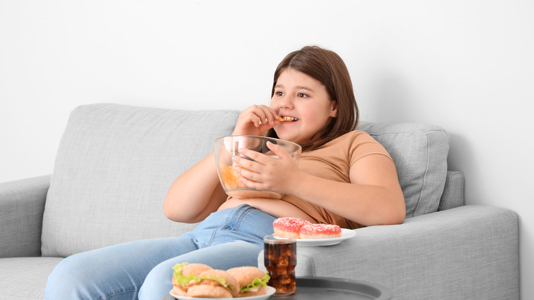 Young heavy girl eating snacks out of a bowl, sitting on couch