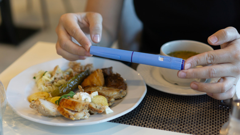 Picture of a woman holding an Ozempic pen over a plate of food