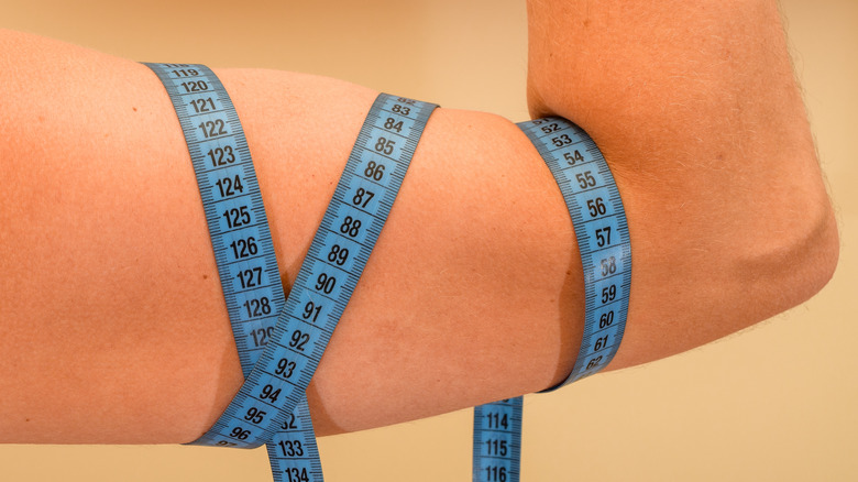 Flexed bicep wrapped in a blue tailor's tape measure